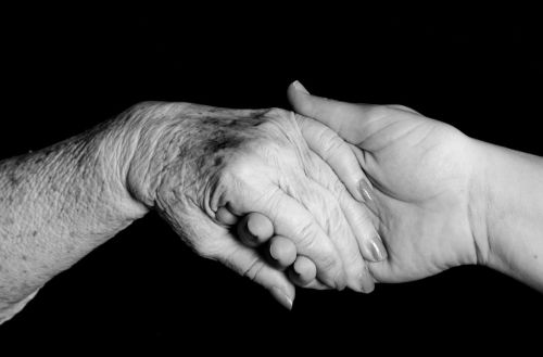 A young woman holding hands with an elderly woman - good care in nursing home concept
